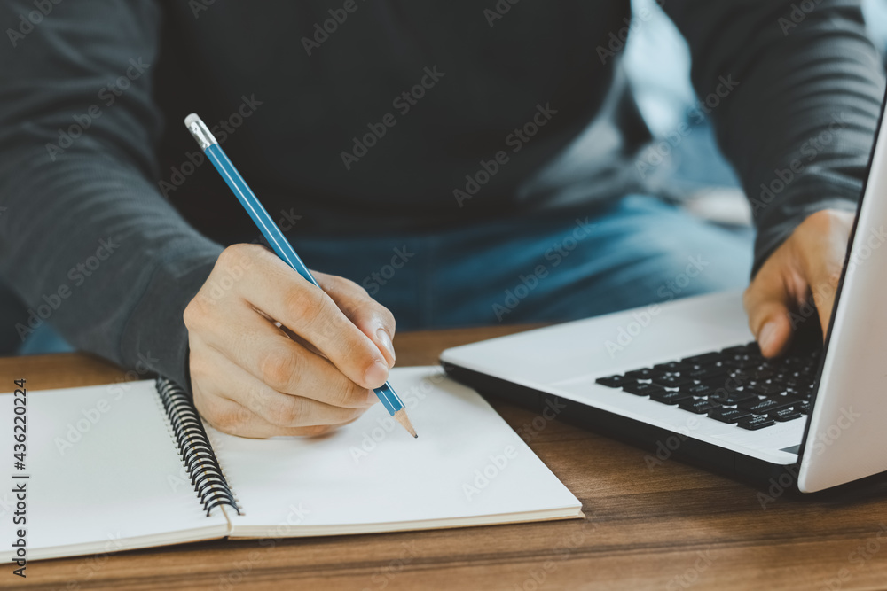 Young man make notes sit at work desk while study online watching webinar podcast on laptop listenin