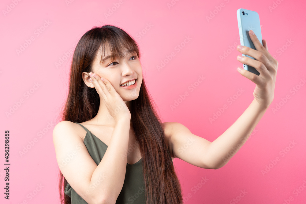 Beautiful young asian girl using phone on pink background