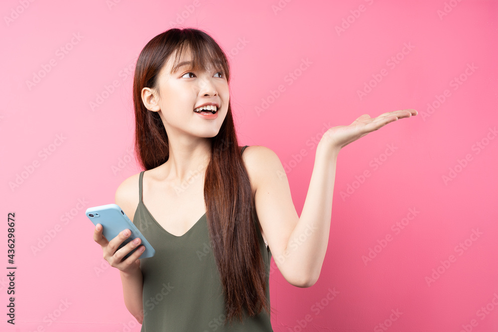 Beautiful young asian girl using phone on pink background