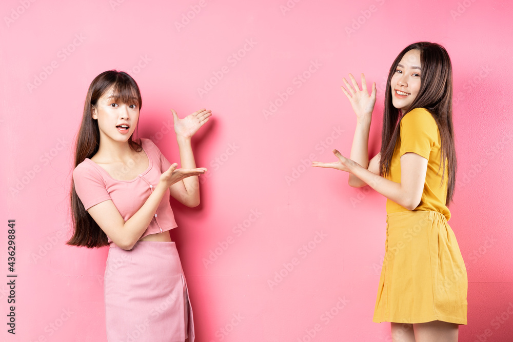 Portrait of two beautiful young Asian girls posing on pink background