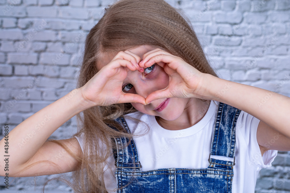 Portrait of girl with blond hair shows heart shape with fingers