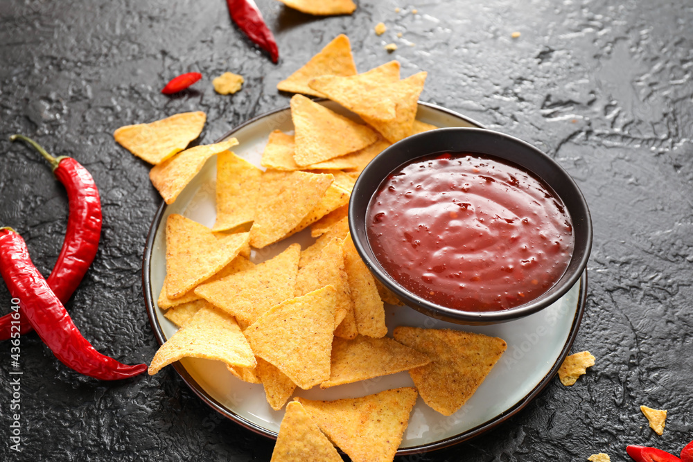 Bowl with tasty chili sauce and nachos on dark background, closeup