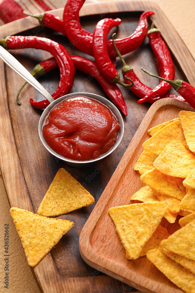 Board with tasty sauce, nachos and chili peppers on color background, closeup