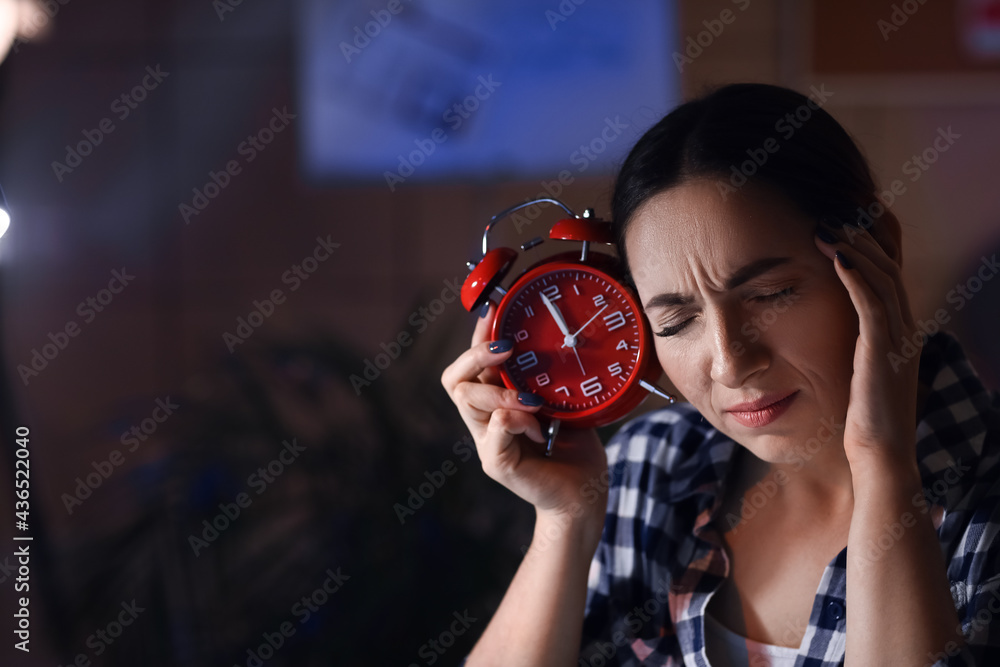 Tired beautiful woman with alarm clock in office at night