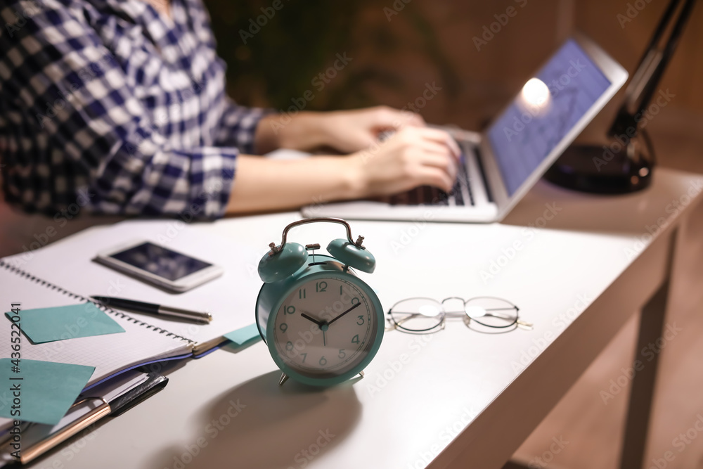 Alarm clock on table of woman working with laptop in evening