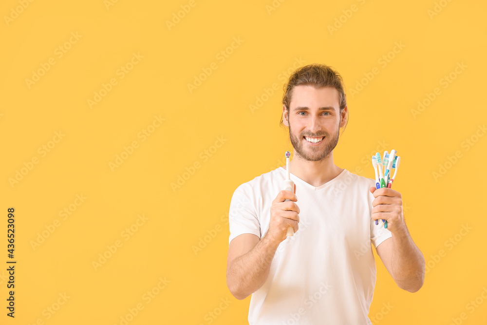 Young man with tooth brushes on color background