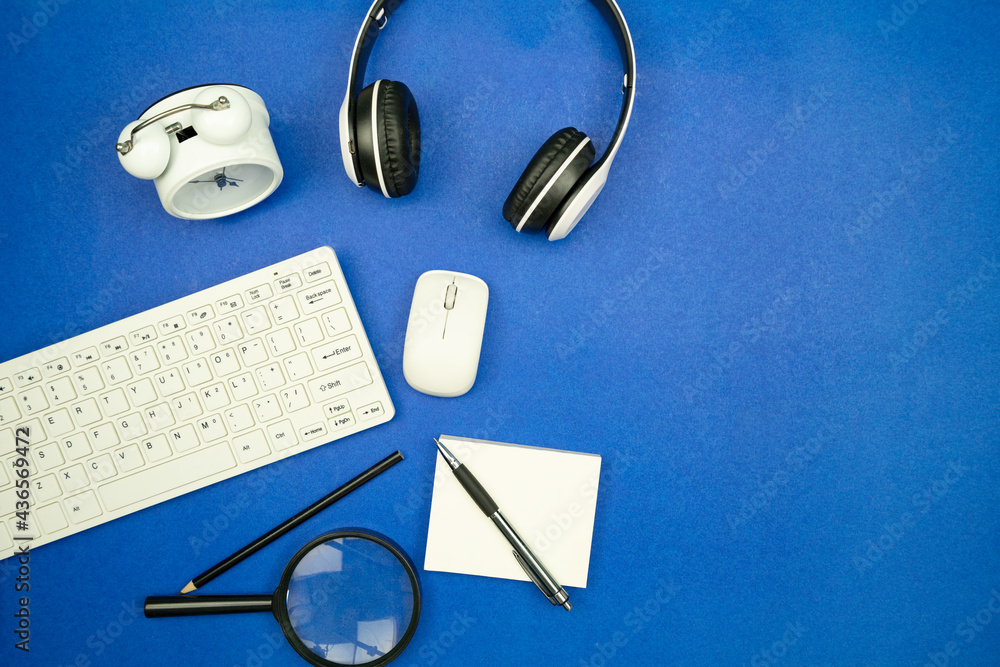 Top view of business objects Keyboard,mouse,Headphone,paperwork with pencil and alarm clock on blue 