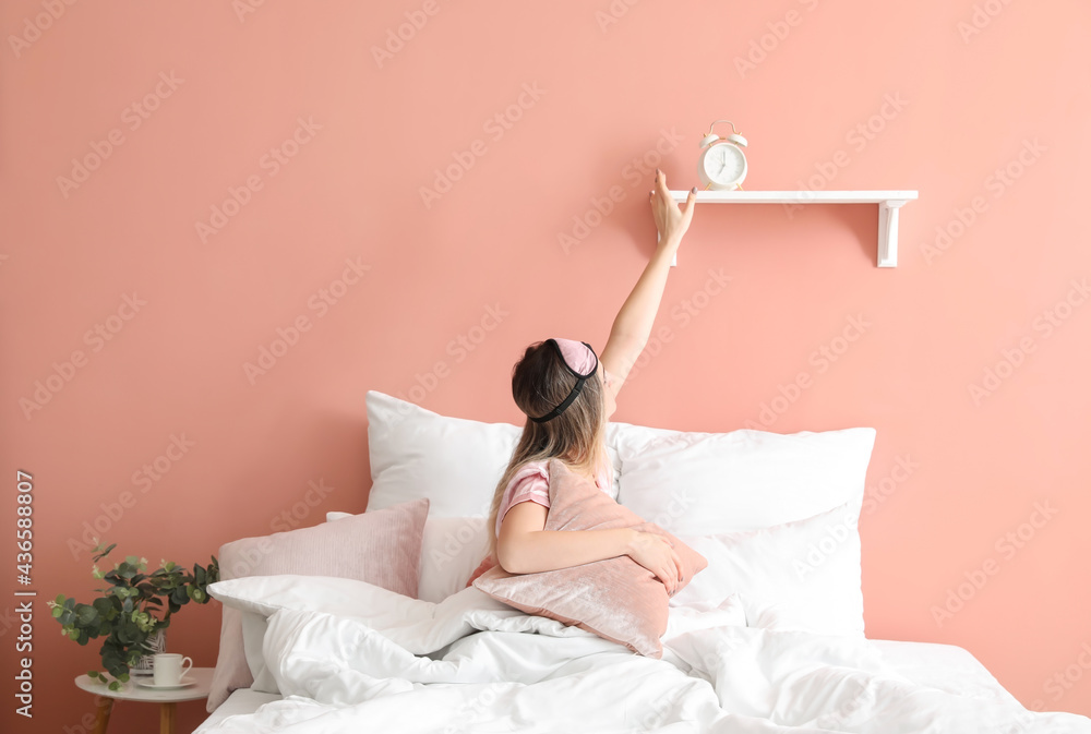 Young woman and alarm clock in bedroom