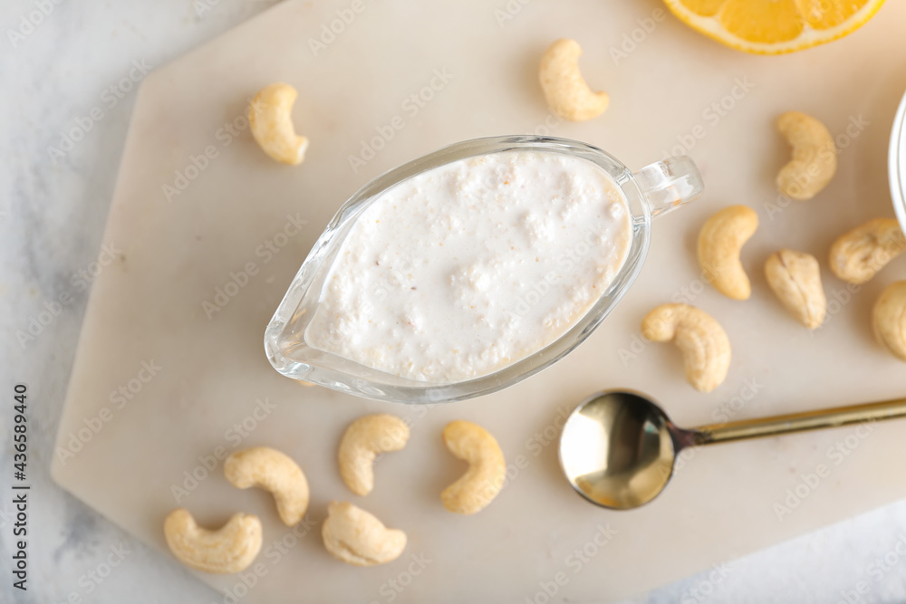 Gravy boat with cashew sour cream and nuts on light background