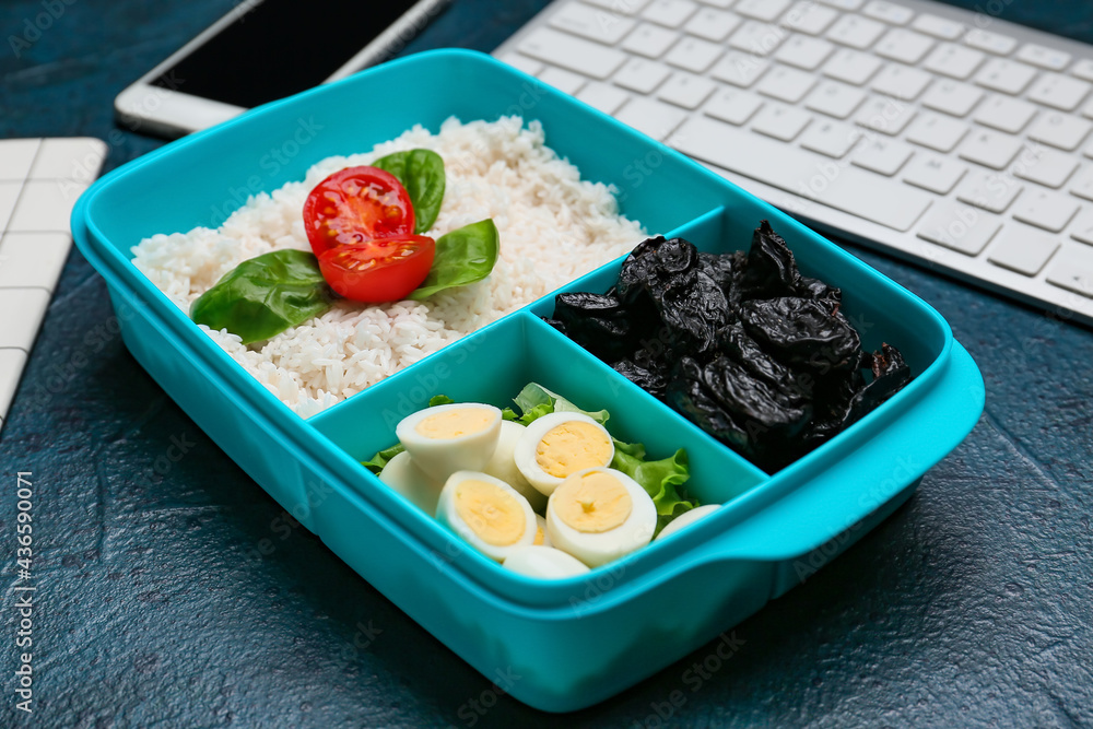 Lunchbox with tasty food and keyboard on dark background