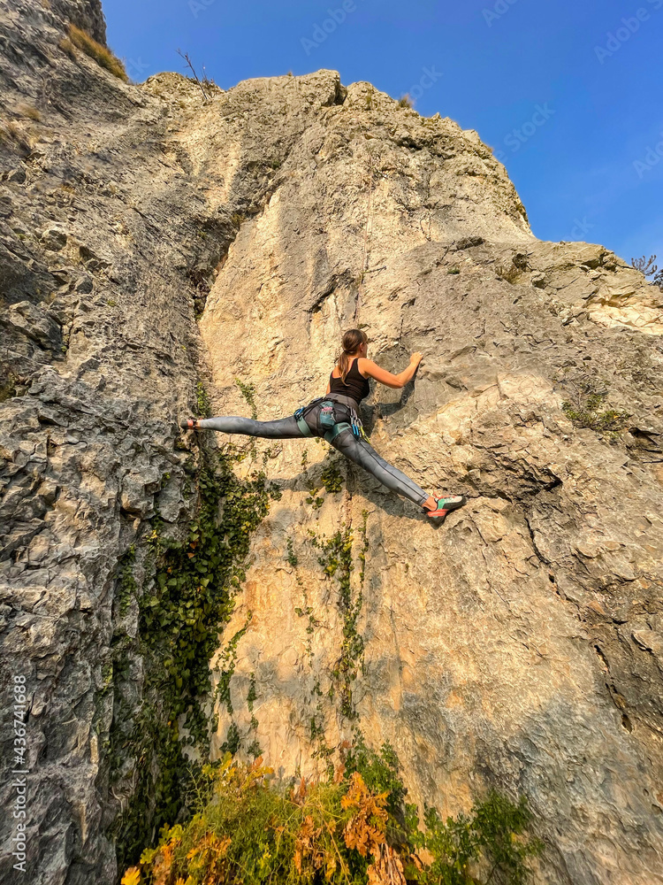 VERTICAL: Agile female rock climber almost does the splits while climbing.