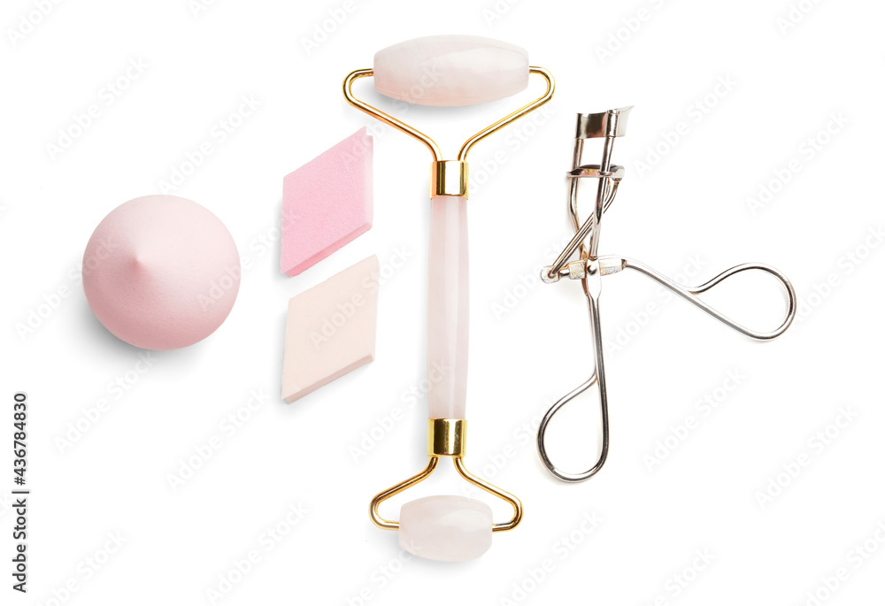 Makeup sponges with massage tool and eyelash curler on white background