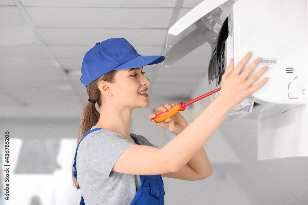 Young female electrician repairing air conditioner in room