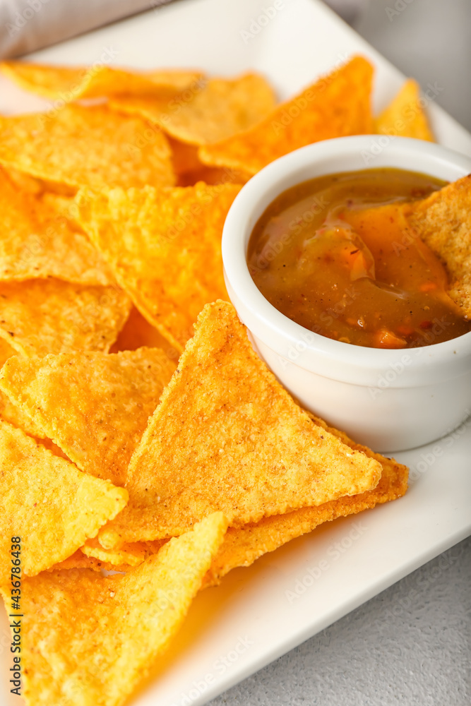 Plate with tasty nachos and sauce on light background