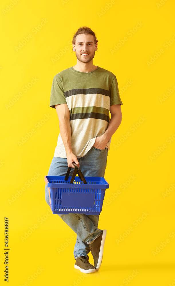 Young man with empty shopping basket on color background