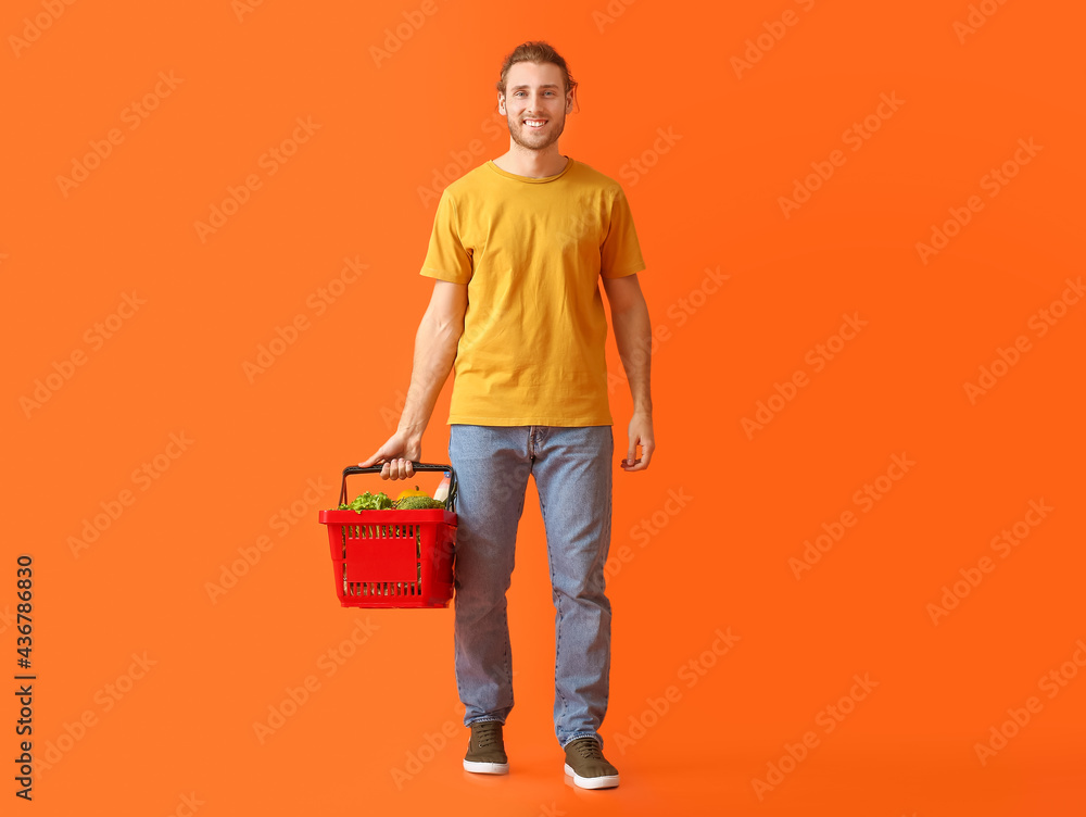 Young man with shopping basket on color background