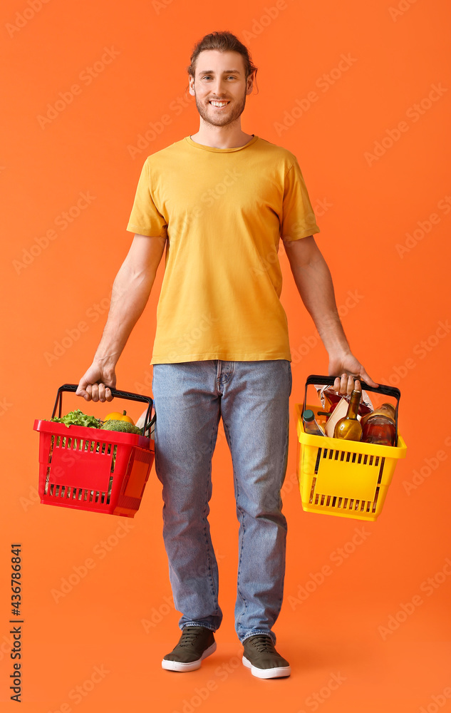 Young man with shopping baskets on color background