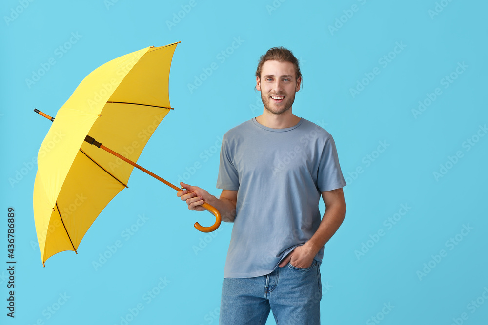 Handsome young man with umbrella on color background