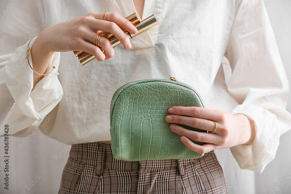 Woman with stylish bag and decorative cosmetics on light background, closeup