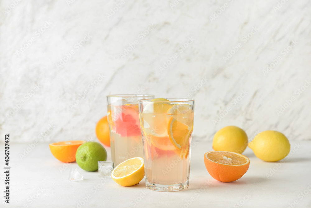 Glasses of tasty cold lemonade and citrus fruits on light background