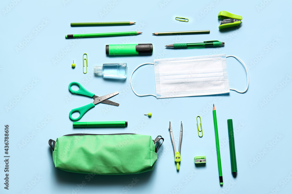 Pencil case with stationery and medical mask on color background