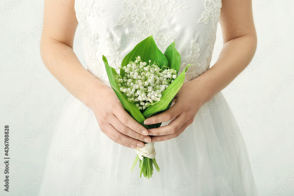 Bride with bouquet of beautiful lily-of-the-valley flowers on light background