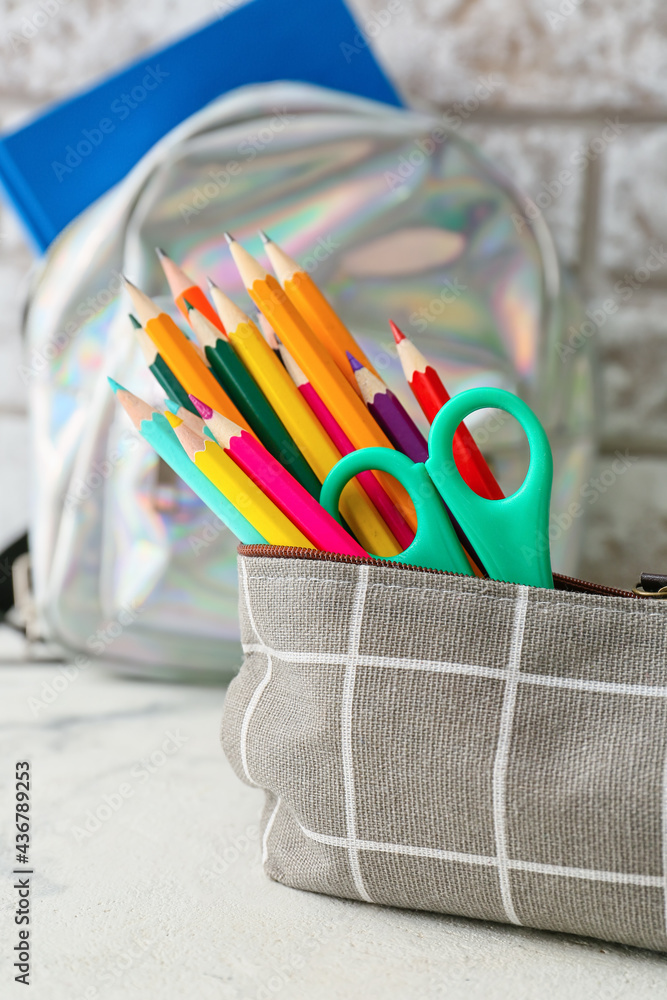 Pencil case and stationery on light table near brick wall