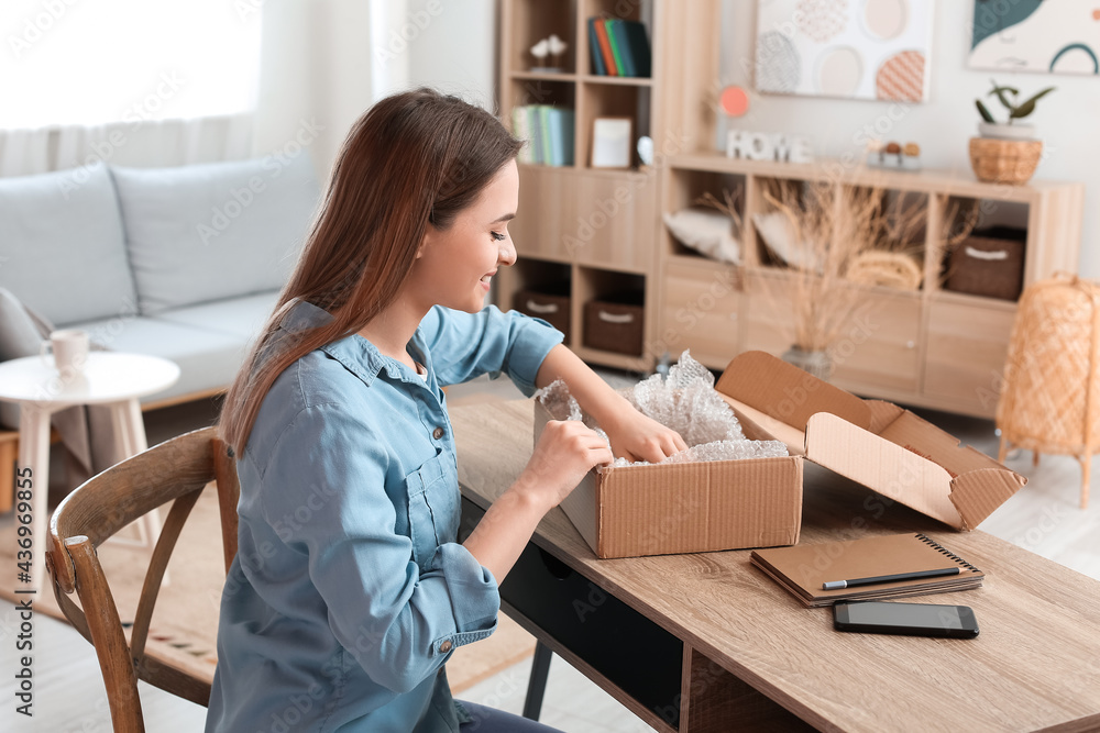 Young woman packing parcel for client at home