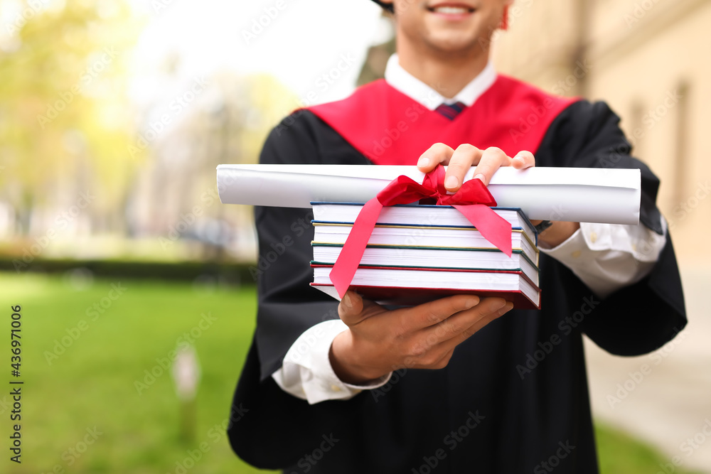 Male graduating student with books outdoors