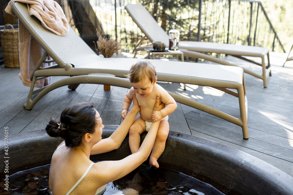 Mom relaxing with a little baby boy at spa resort, sitting in the hot vat outdoors. Family on vacati