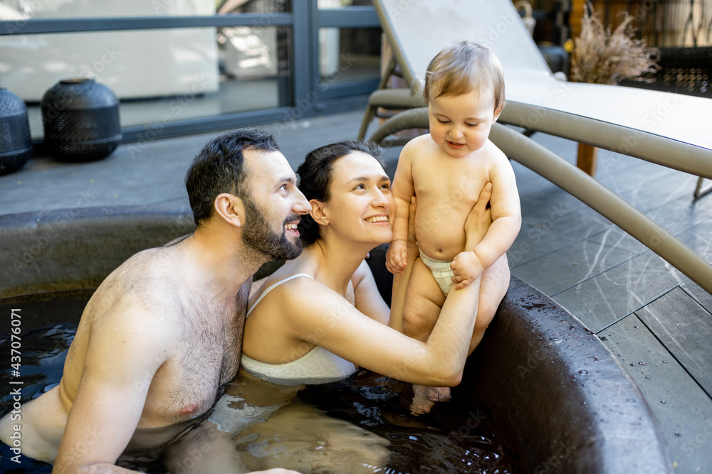 Young family relaxing with a little baby boy at spa, sitting in the hot vat outdoors. Family on vaca