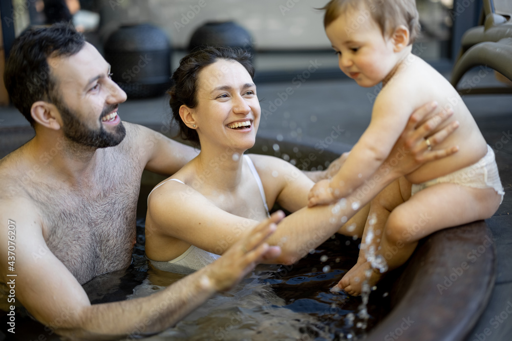 Young family relaxing with a little baby boy at spa, sitting in the hot vat outdoors. Family on vaca