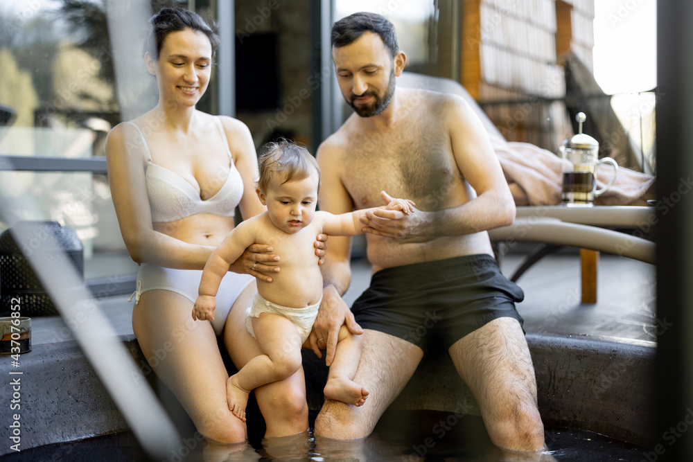 Young family relaxing with a little baby boy at spa, sitting in the hot vat outdoors. Family on vaca