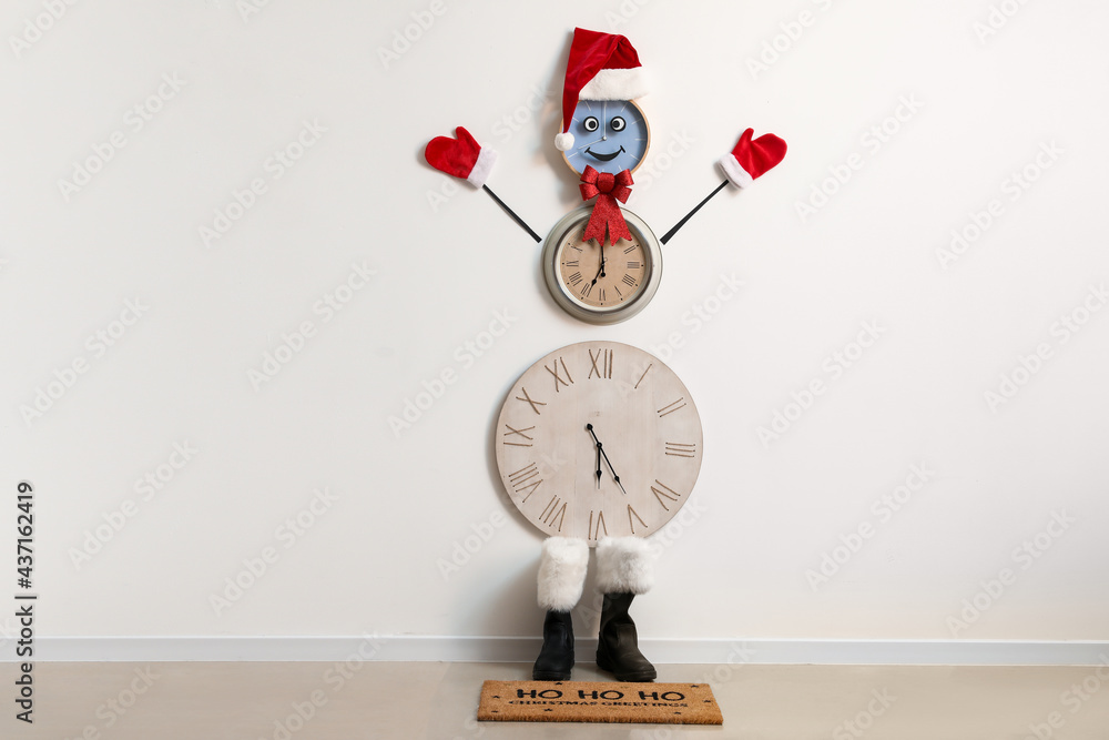 Funny snowman made of clocks near white wall