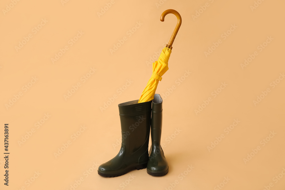 Stylish umbrella and rubber boots on color background