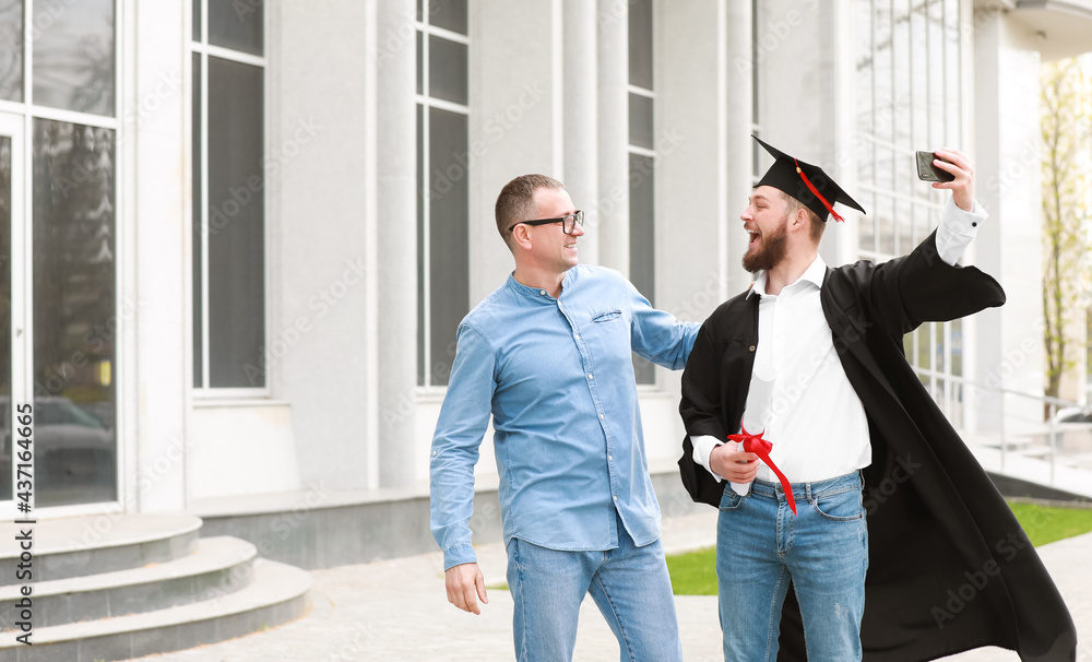 Happy young man with his father taking selfie on graduation day