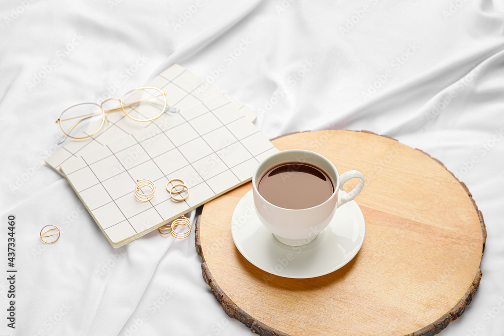 Board with cup of coffee and notebooks with accessory on bed