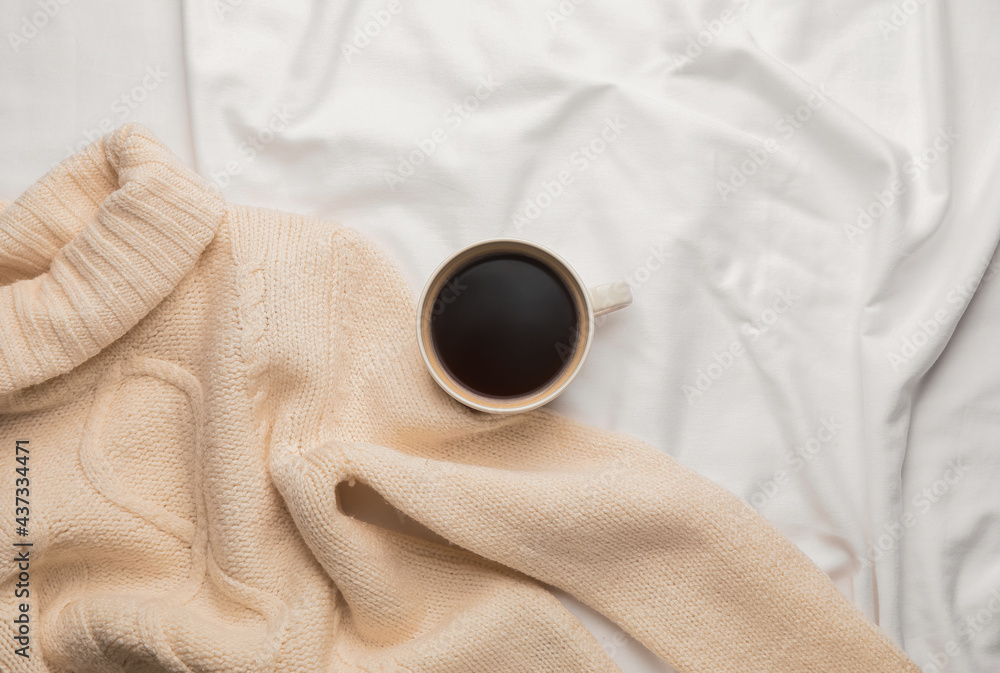 Cup of coffee and sweater on bed