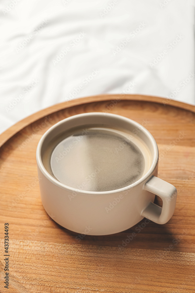 Wooden tray with cup of coffee on bed, closeup