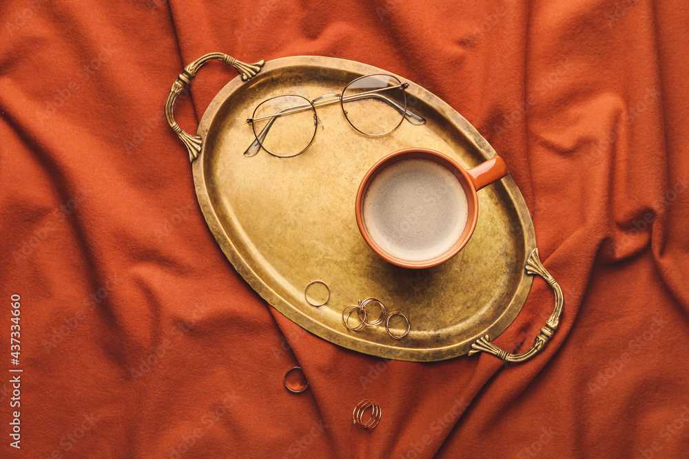 Tray with cup of coffee, female accessories and glasses on bed