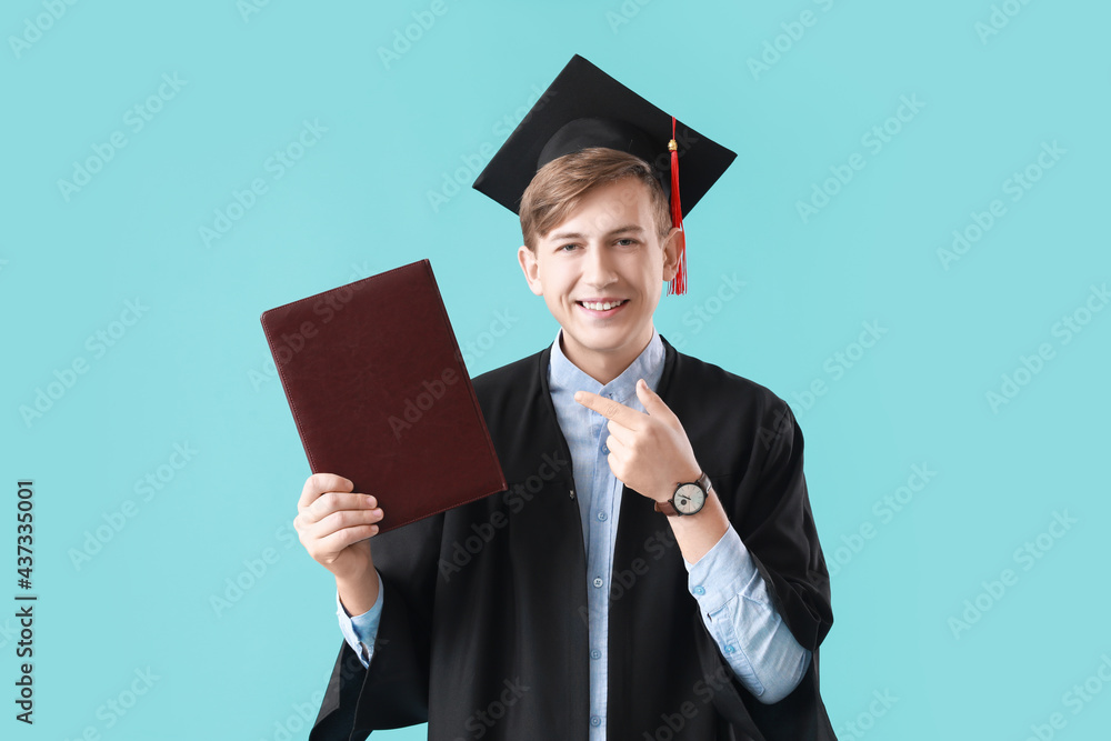 Male graduating student with book on color background