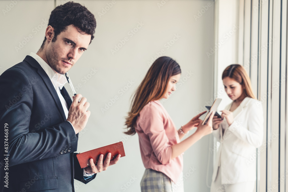 Happy young handsome businessman reading book and working in office with colleagues and friend at wo