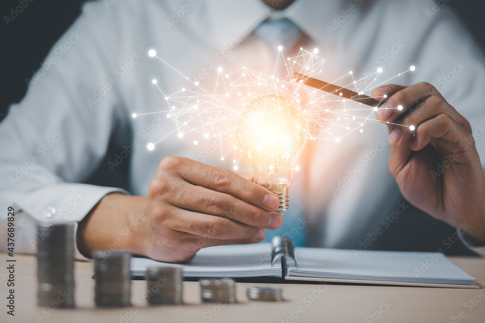 Businessman pen touch light bulb with line connect and Coins stack on the wooden table, Saving ideas