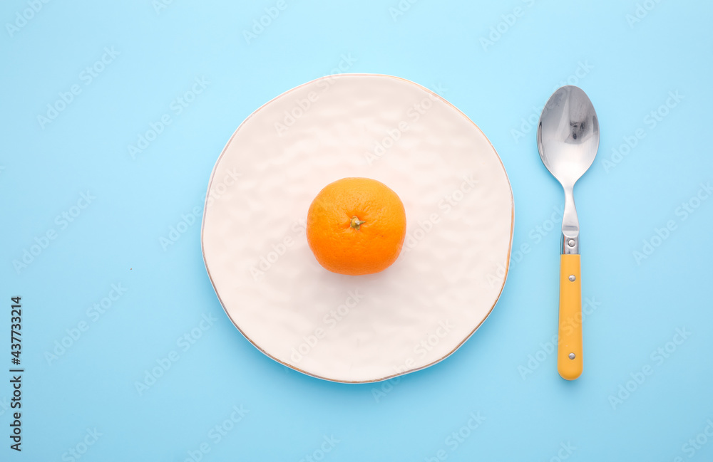 Clean spoon with plate and tangerine on color background