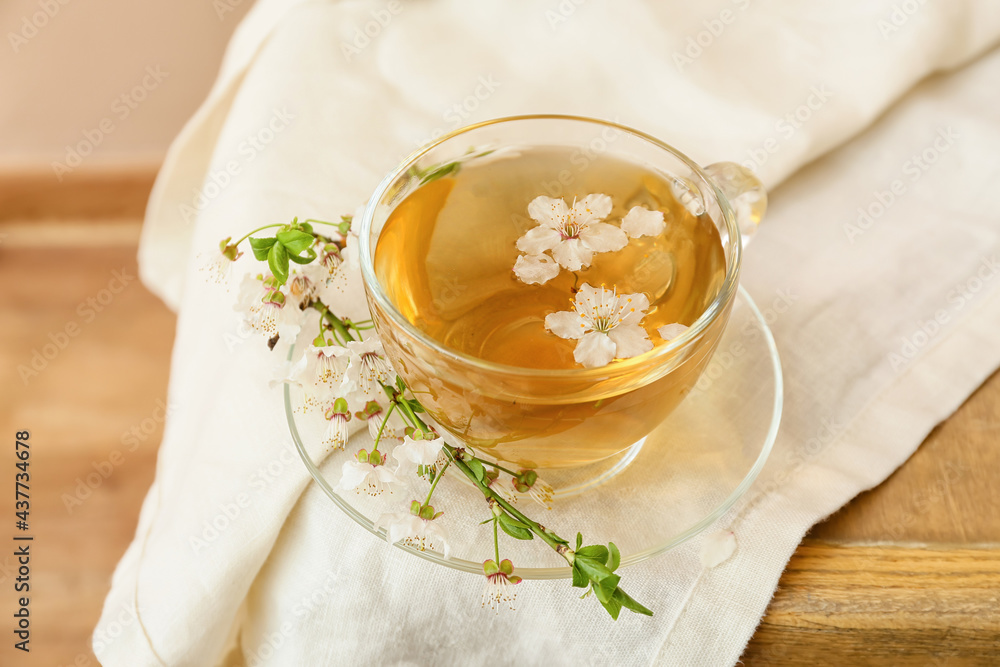 Cup with tasty tea and blooming branch on wooden background