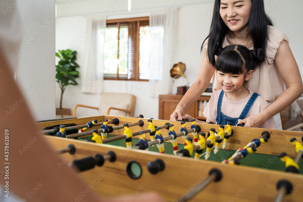 年轻的女孩、孩子、女儿在家和父母玩桌上足球玩得很开心