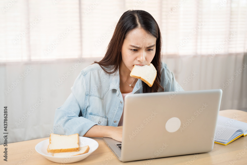 饥饿的女商人在电脑上工作时匆匆忙忙地吃面包。