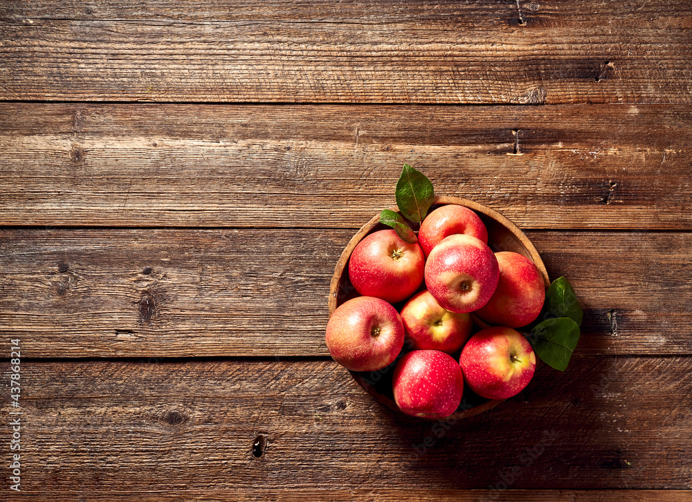 Ripe apples on old wooden background with apple leaves.