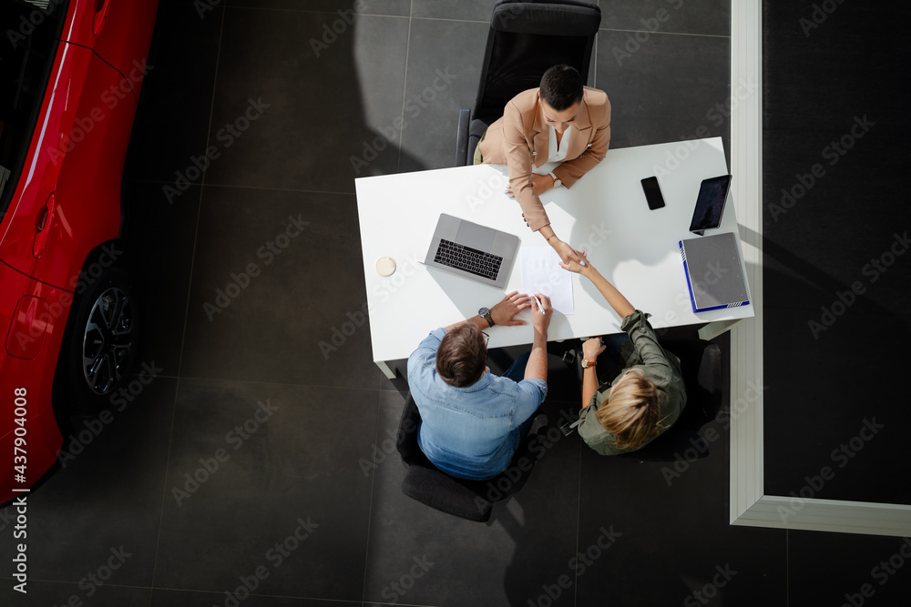 Top view of female customer receiving car keys, shaking hands with saleswoman.