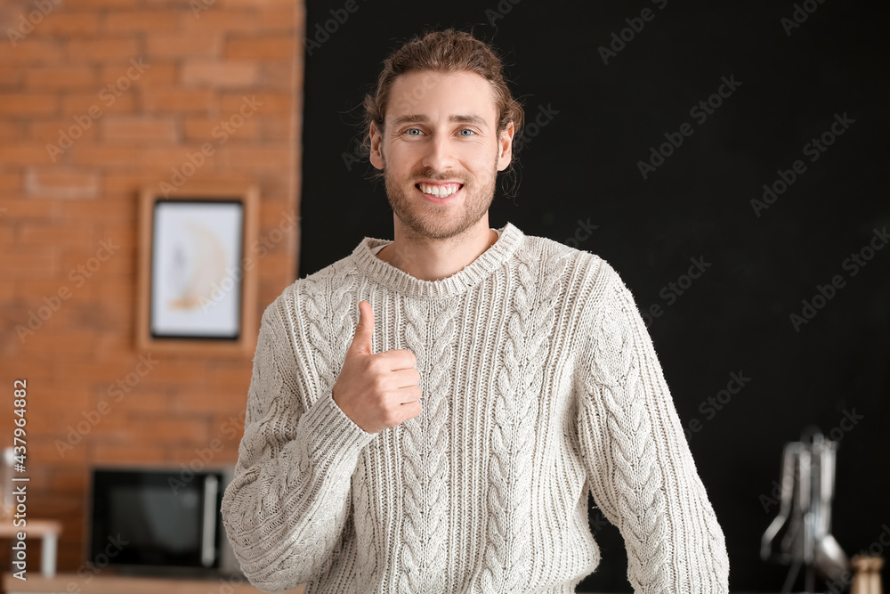 Smiling young man showing thumb-up at home